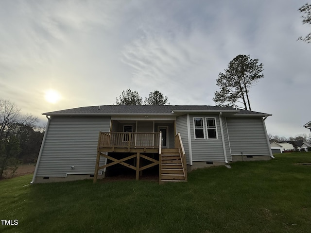 back house at dusk featuring a deck and a lawn