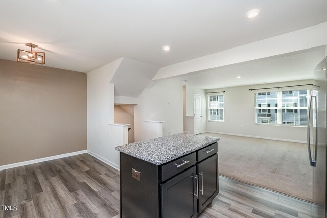 kitchen with hardwood / wood-style flooring, a kitchen island, stainless steel refrigerator, and light stone countertops