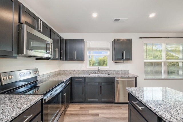 kitchen featuring sink, light stone countertops, appliances with stainless steel finishes, and light hardwood / wood-style floors