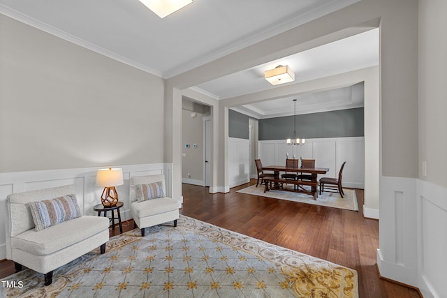 sitting room with dark wood-type flooring, ornamental molding, and an inviting chandelier