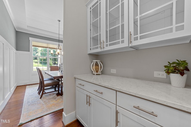 kitchen with light stone countertops, a notable chandelier, ornamental molding, hardwood / wood-style flooring, and white cabinetry