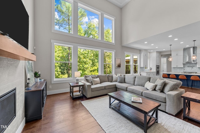 living room with dark hardwood / wood-style floors, a towering ceiling, a wealth of natural light, and a tile fireplace