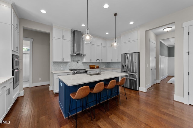 kitchen featuring wall chimney exhaust hood, appliances with stainless steel finishes, an island with sink, dark wood-type flooring, and white cabinets