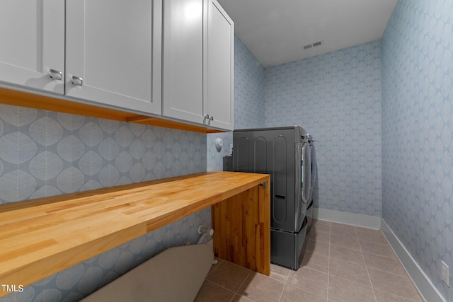 clothes washing area featuring light tile patterned floors, washing machine and clothes dryer, and cabinets