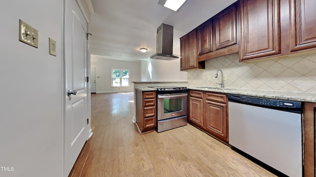 kitchen featuring light wood-type flooring, appliances with stainless steel finishes, wall chimney exhaust hood, and light stone counters