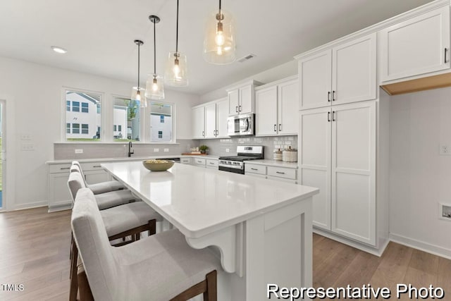 kitchen with appliances with stainless steel finishes, light hardwood / wood-style floors, white cabinetry, pendant lighting, and a center island