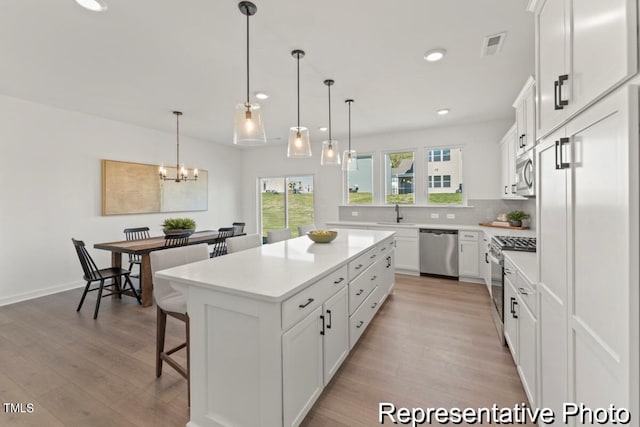 kitchen with appliances with stainless steel finishes, hanging light fixtures, light hardwood / wood-style floors, white cabinets, and a kitchen island