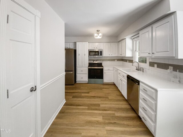 kitchen featuring appliances with stainless steel finishes, backsplash, sink, light wood-type flooring, and white cabinets