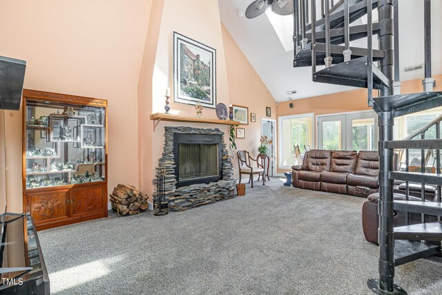 carpeted living room with ceiling fan, a stone fireplace, and high vaulted ceiling