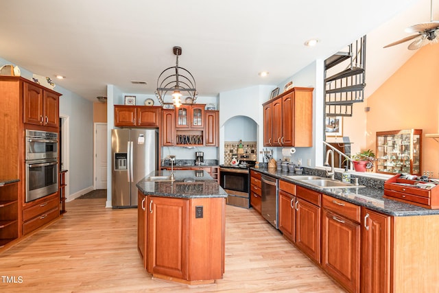 kitchen featuring ceiling fan with notable chandelier, light hardwood / wood-style floors, stainless steel appliances, and a center island with sink