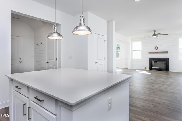 kitchen with dark wood-style flooring, hanging light fixtures, light countertops, a glass covered fireplace, and a center island