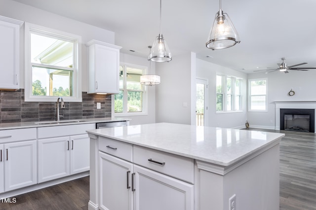 kitchen with a sink, dark wood-type flooring, white cabinets, a glass covered fireplace, and backsplash