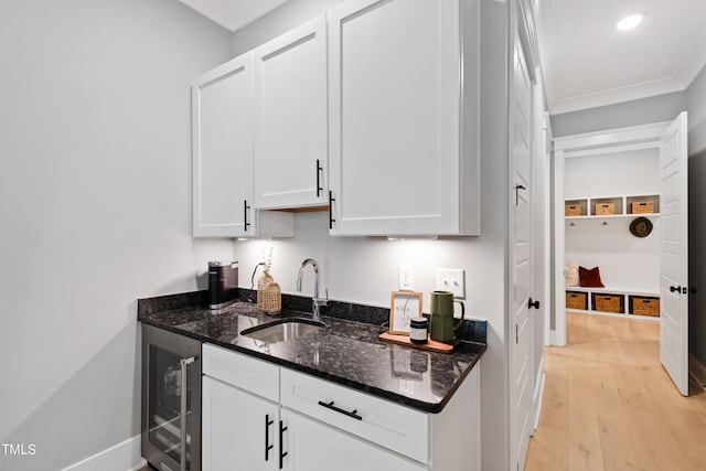 kitchen featuring dark stone countertops, white cabinets, beverage cooler, light hardwood / wood-style flooring, and sink