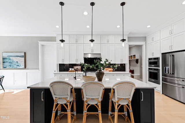 kitchen featuring hanging light fixtures, a center island with sink, stainless steel appliances, and white cabinets