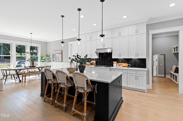 kitchen featuring light hardwood / wood-style floors, white cabinetry, a center island with sink, and hanging light fixtures