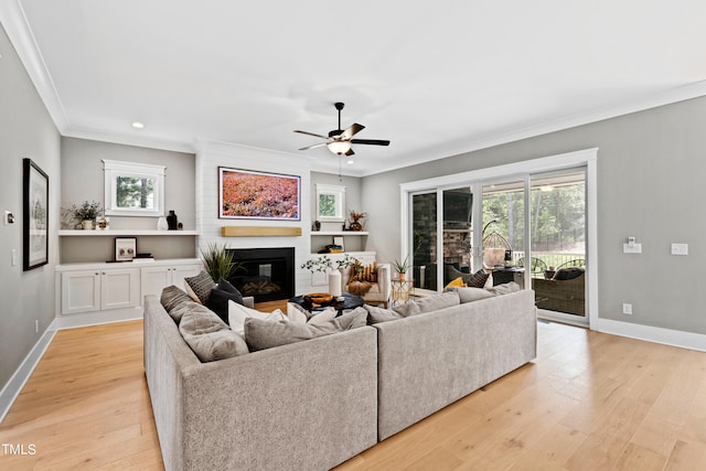 living room featuring ceiling fan, ornamental molding, a fireplace, and light hardwood / wood-style floors