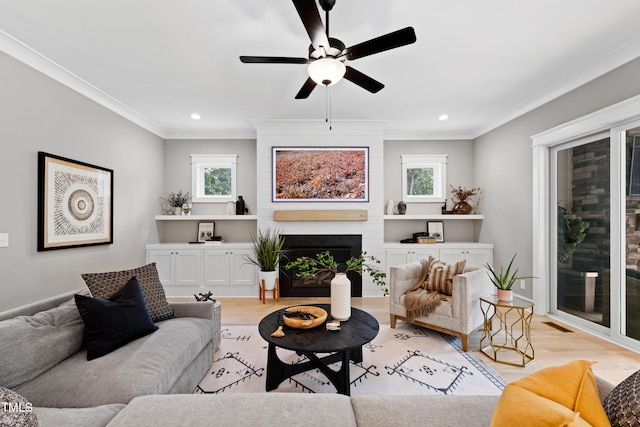 living room with ceiling fan, light hardwood / wood-style flooring, ornamental molding, and a large fireplace