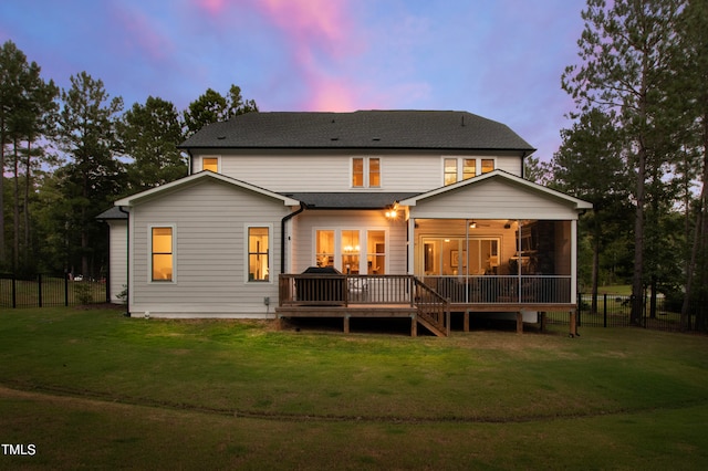 back house at dusk with a wooden deck and a yard