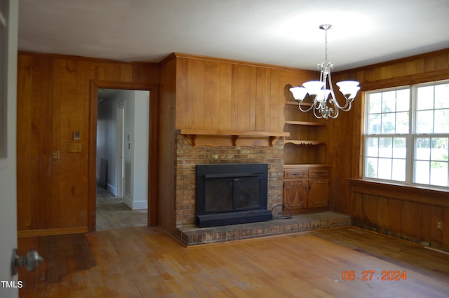 unfurnished living room featuring a fireplace, hardwood / wood-style floors, a notable chandelier, and wooden walls