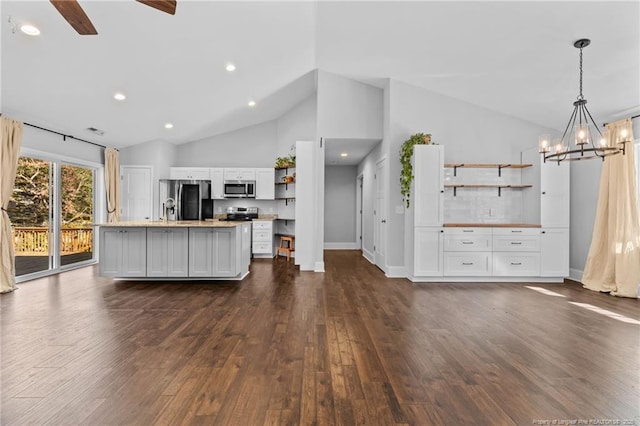 kitchen with dark wood-type flooring, white cabinetry, pendant lighting, stainless steel appliances, and a kitchen island with sink