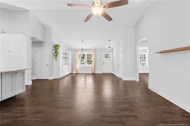 unfurnished living room with ceiling fan with notable chandelier, dark wood-type flooring, and high vaulted ceiling