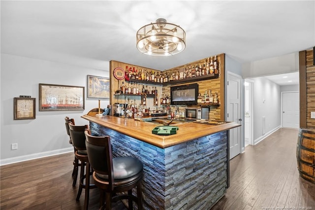 bar featuring butcher block counters, dark wood-type flooring, and a notable chandelier