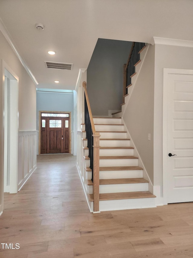 entrance foyer with ornamental molding, wainscoting, wood finished floors, and visible vents