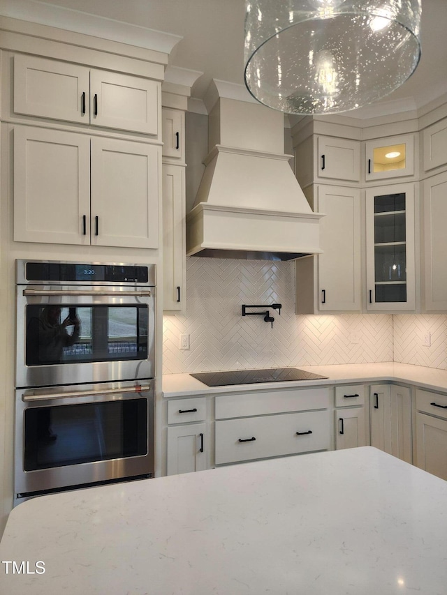 kitchen with double oven, premium range hood, backsplash, and glass insert cabinets