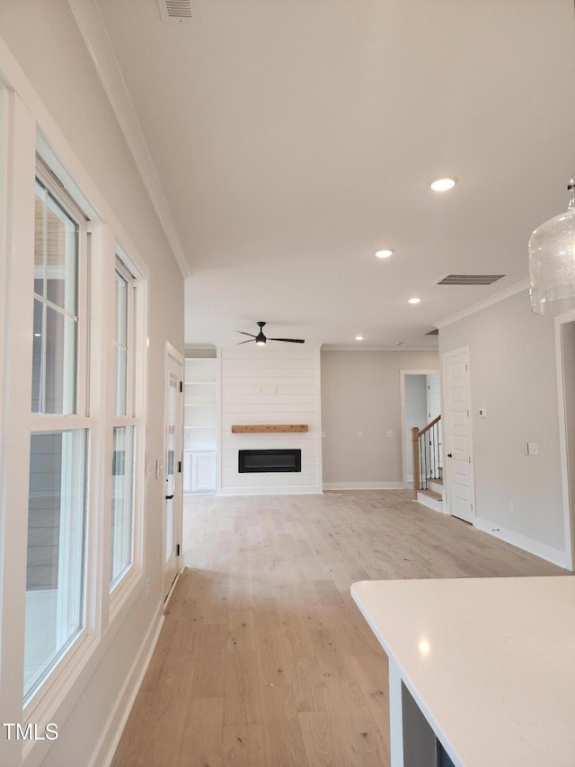 unfurnished living room featuring ornamental molding, a large fireplace, light wood finished floors, and stairs