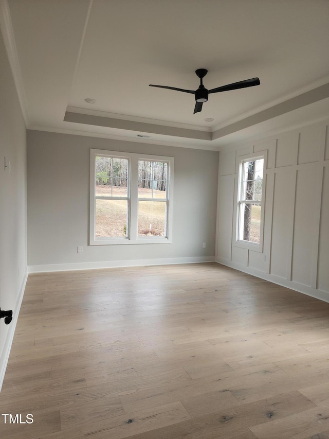 empty room with light wood-style flooring, a tray ceiling, ceiling fan, and crown molding