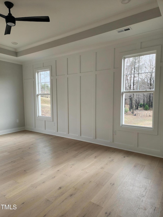 unfurnished bedroom with light wood-style floors, a raised ceiling, visible vents, and a decorative wall