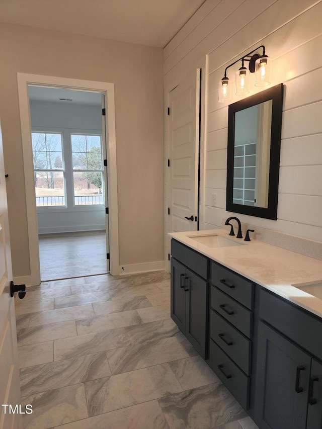 full bath with double vanity, baseboards, marble finish floor, wood walls, and a sink