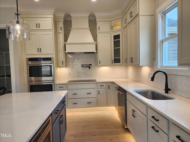 kitchen featuring premium range hood, a sink, hanging light fixtures, ornamental molding, and appliances with stainless steel finishes