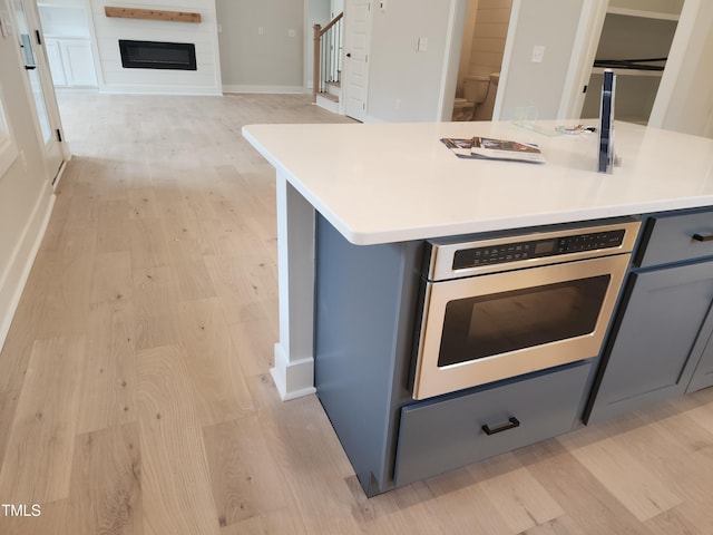 kitchen with wall oven, light wood-type flooring, light countertops, and gray cabinetry