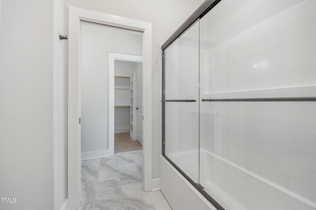 bathroom featuring marble finish floor, shower / bath combination with glass door, a walk in closet, and baseboards