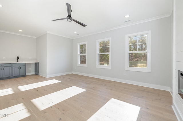 unfurnished living room with a healthy amount of sunlight, light wood-style flooring, visible vents, and ornamental molding