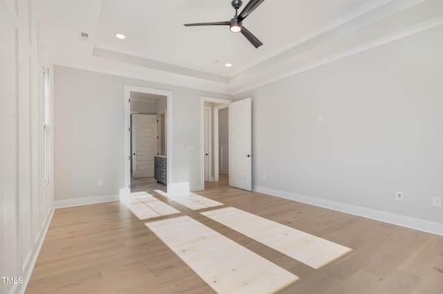 unfurnished bedroom featuring light wood-style flooring, a tray ceiling, and baseboards