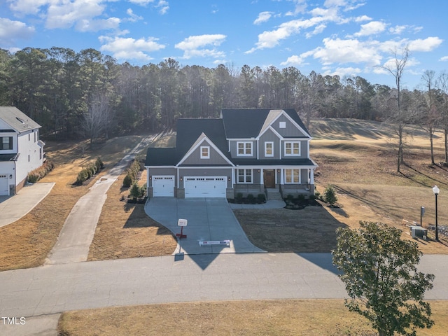 view of front facade featuring a garage, concrete driveway, covered porch, and a wooded view