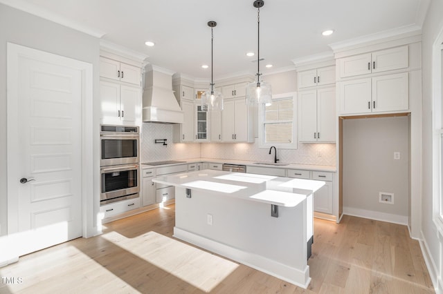 kitchen with stainless steel appliances, a sink, white cabinetry, light countertops, and custom range hood