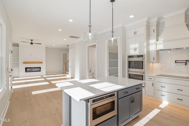 kitchen featuring a fireplace, stainless steel appliances, custom range hood, light wood-style flooring, and gray cabinetry