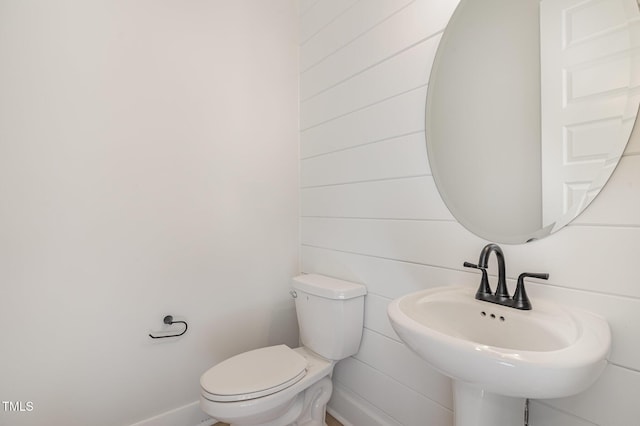 half bath with toilet, baseboards, and a sink