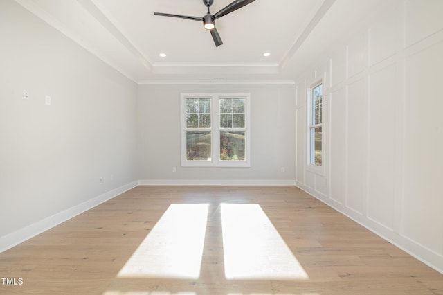 empty room with light wood-type flooring, baseboards, a raised ceiling, and ornamental molding