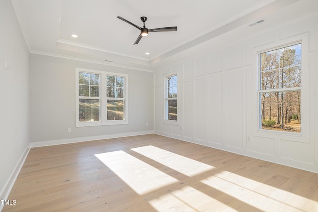 unfurnished room with a wealth of natural light, a raised ceiling, a decorative wall, and light wood finished floors