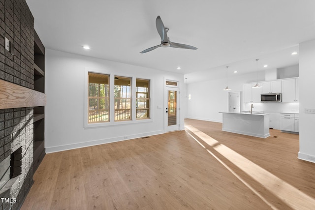 unfurnished living room featuring light wood-style flooring, ceiling fan, a brick fireplace, a sink, and recessed lighting