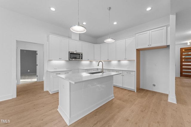 kitchen with an island with sink, stainless steel microwave, decorative backsplash, and a sink