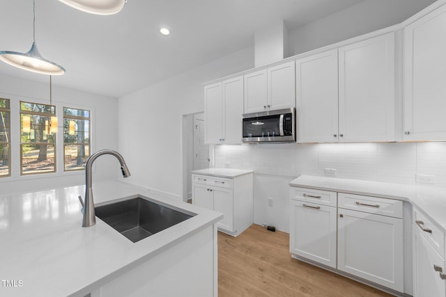 kitchen with tasteful backsplash, white cabinets, stainless steel microwave, light wood-style floors, and a sink