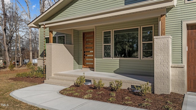 doorway to property with a porch and brick siding