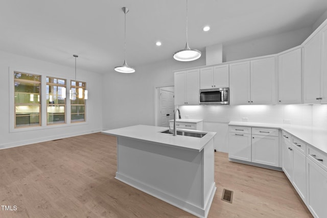 kitchen featuring stainless steel microwave, decorative light fixtures, a sink, light wood-style floors, and backsplash