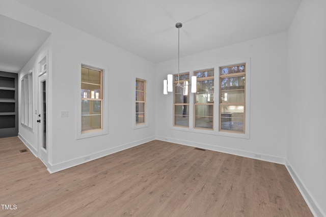 unfurnished dining area featuring visible vents, a notable chandelier, baseboards, and wood finished floors