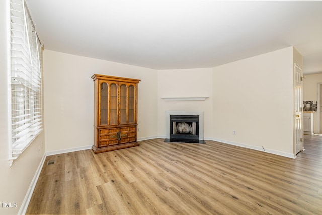 unfurnished living room with a fireplace with flush hearth, visible vents, baseboards, and light wood-style flooring